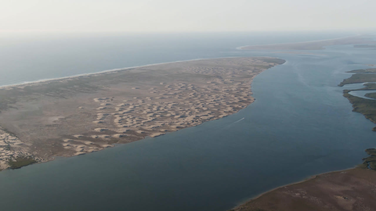 Aerial view over Aldofo Lopez Mateos, Baja California Sur, with a wide water channel, pale sand banks, ocean beach at left, hazy horizon, and no visible people.