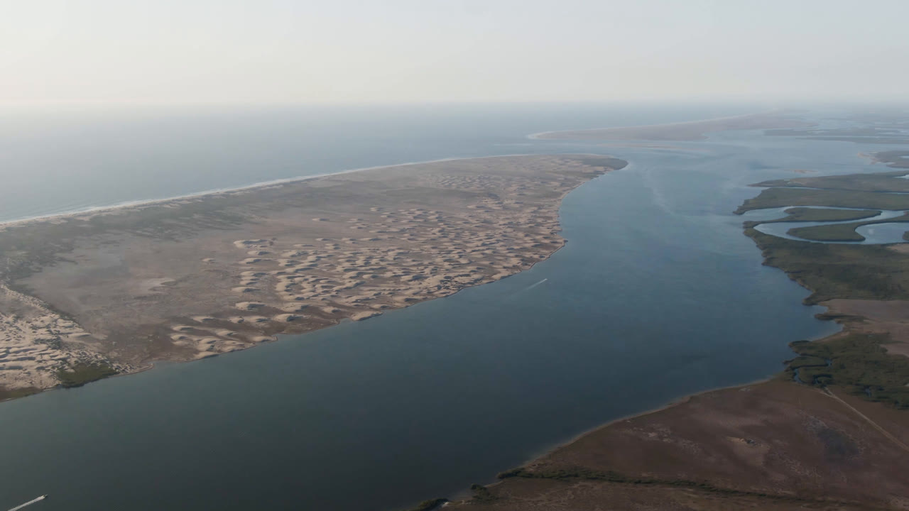Wide aerial view of a coastal inlet with beach and marshland.