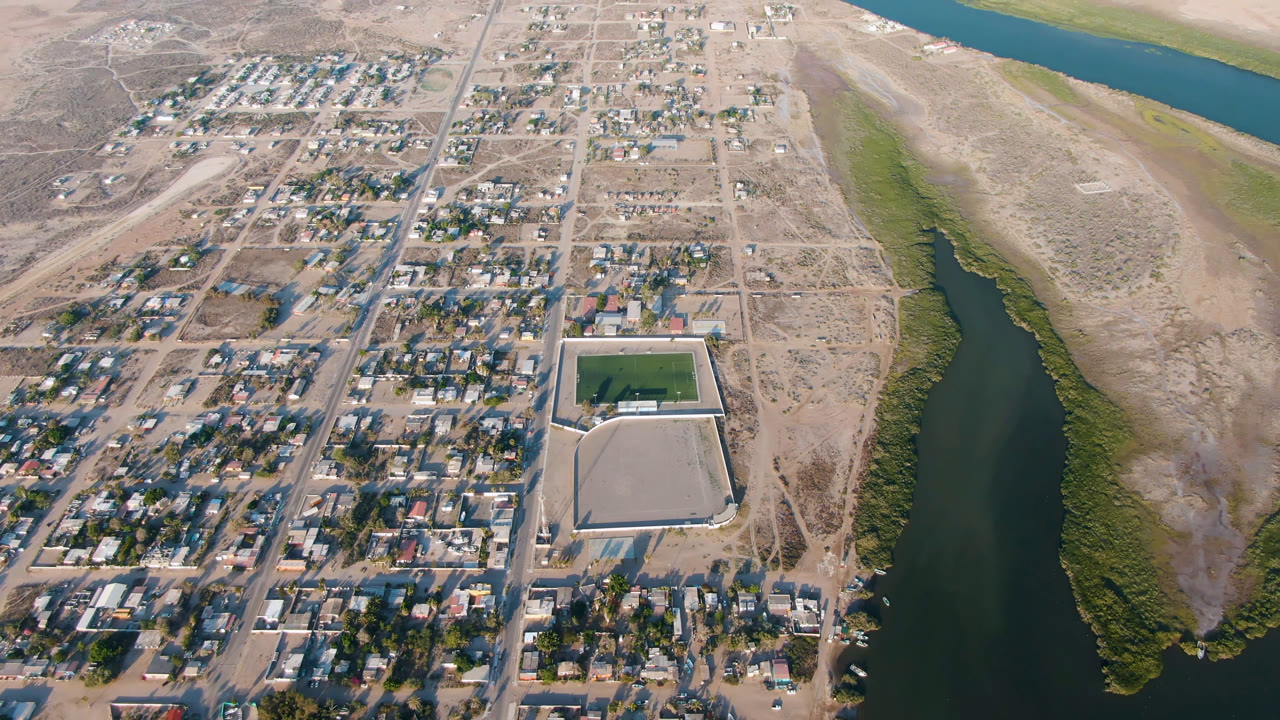 Aerial view of a dry town beside a river channel and mangroves.
