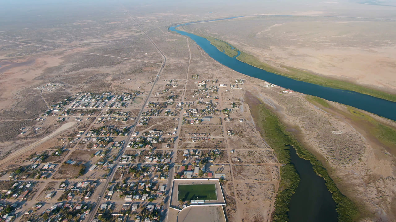 High aerial view of a dry town beside a blue river and desert flats.