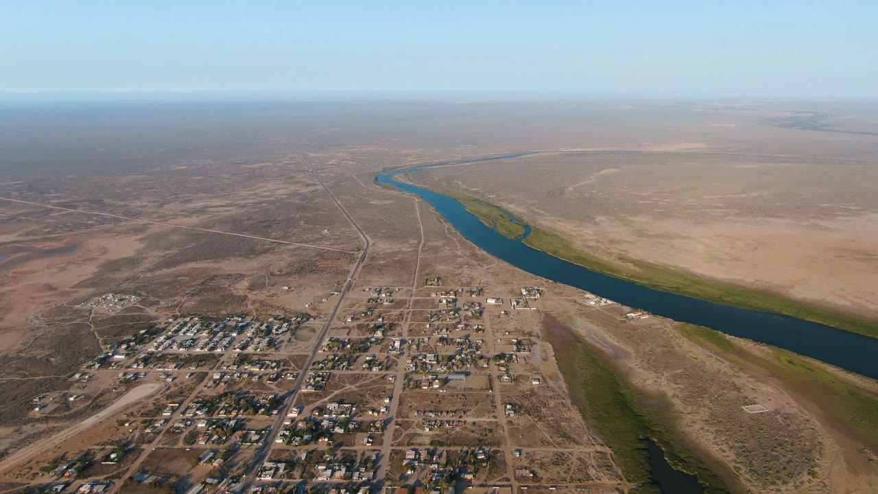 Drone-height view of a town edge, river channel, and broad desert flats.