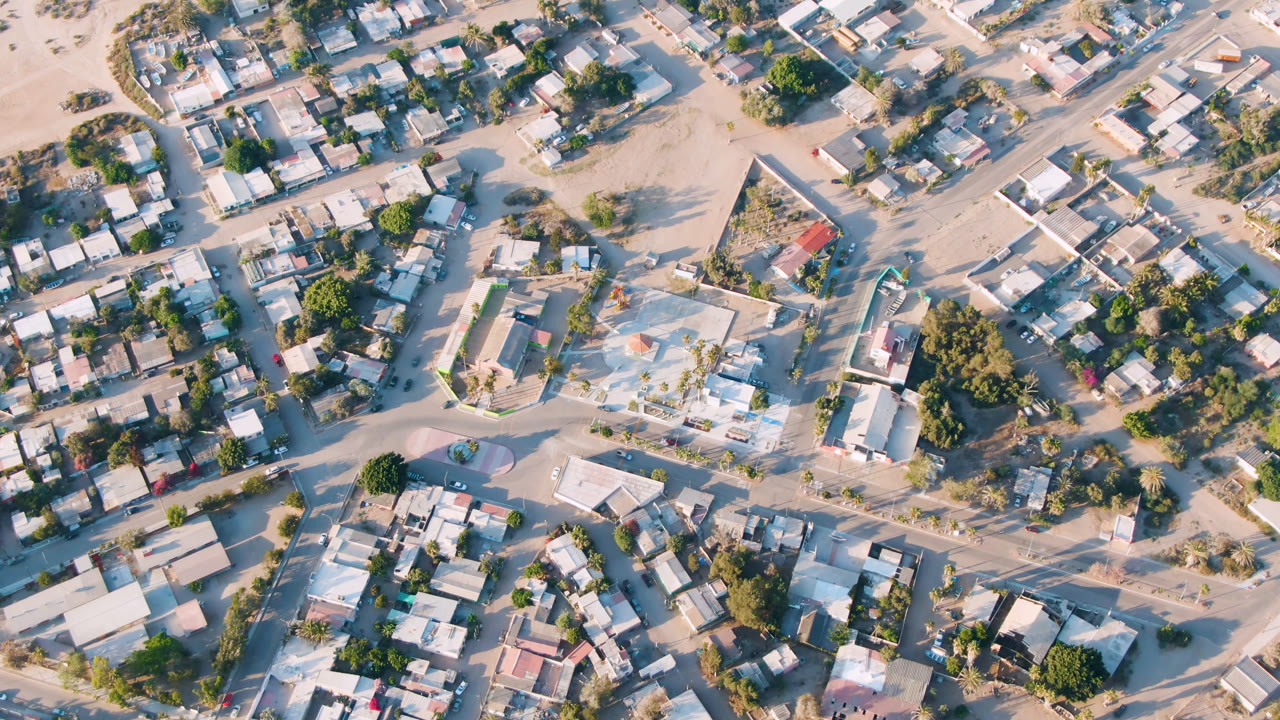 Top-down town view with homes, trees, and a larger light-roofed building near sandy streets.