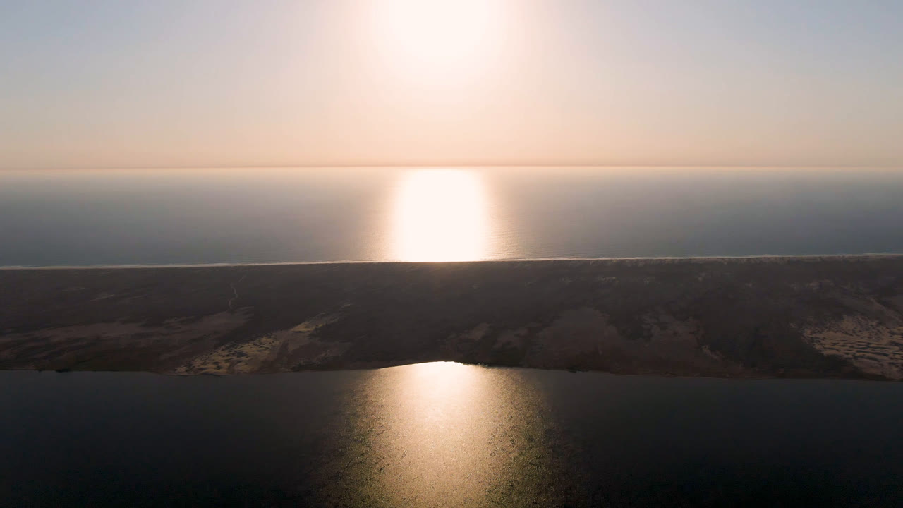 Aerial view in Aldofo Lopez Mateos, Baja California Sur, showing the reflected sun shifted across the water, the long dark shoreline strip, and no visible people.