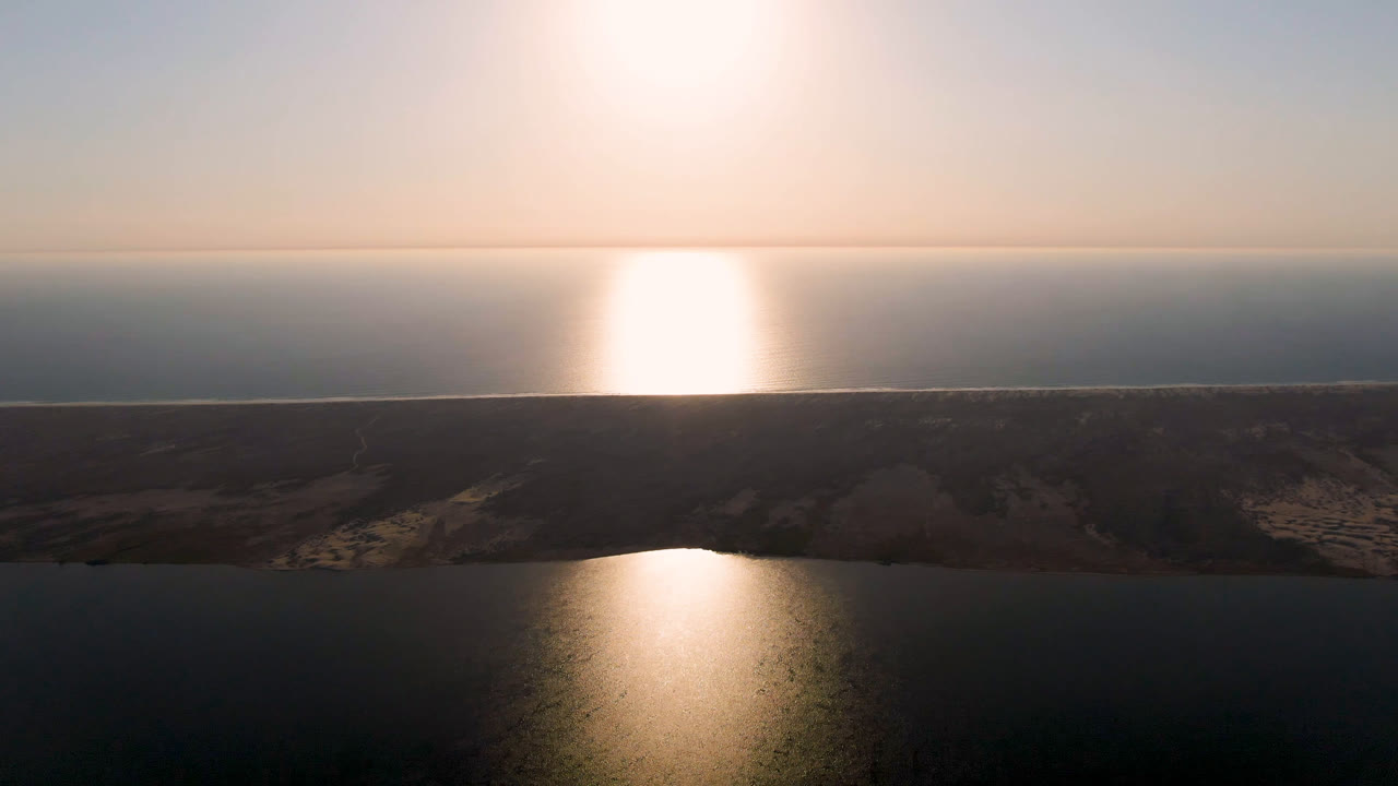 Wide aerial water and shoreline with bright glare near the horizon.