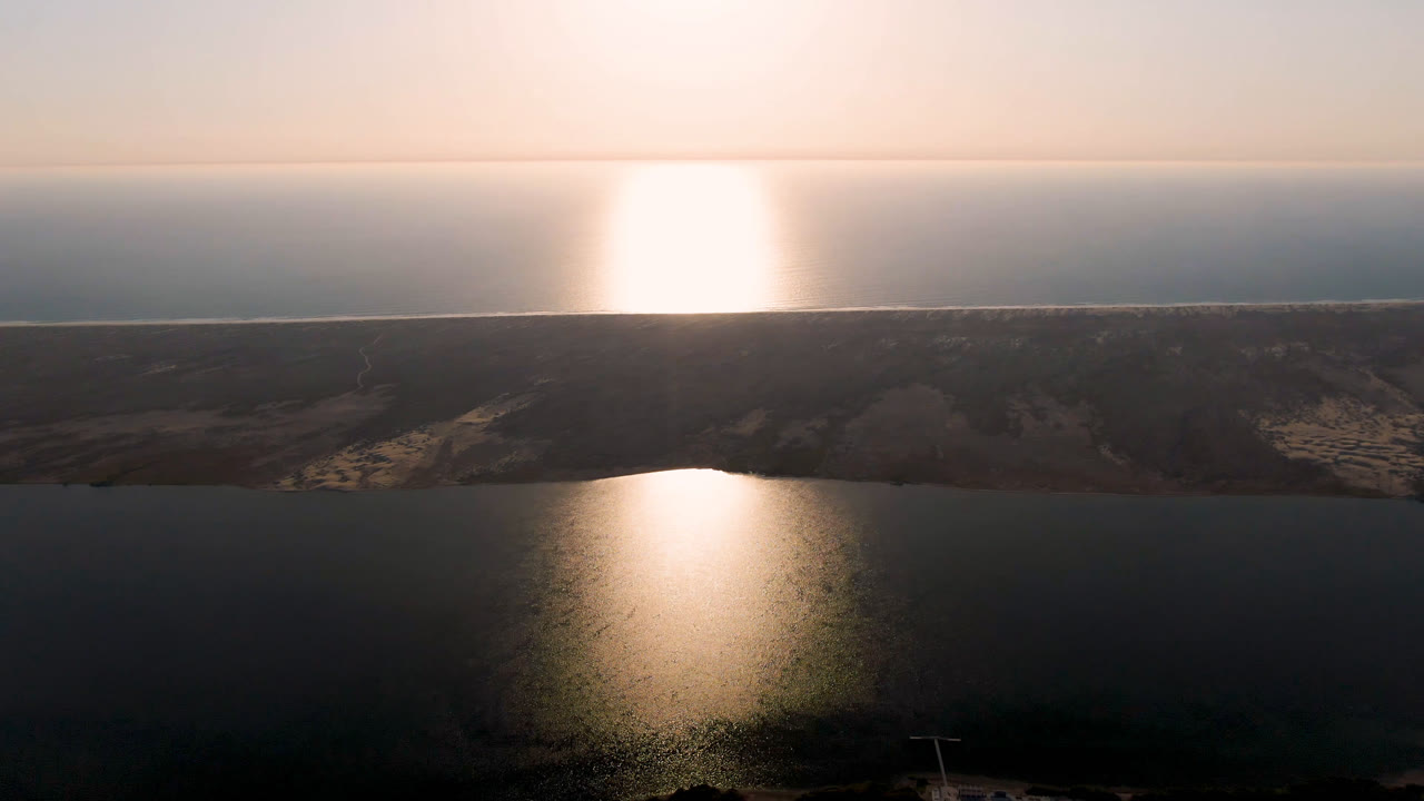 Aerial view of dark water, low shoreline, and bright sun glare near the horizon.