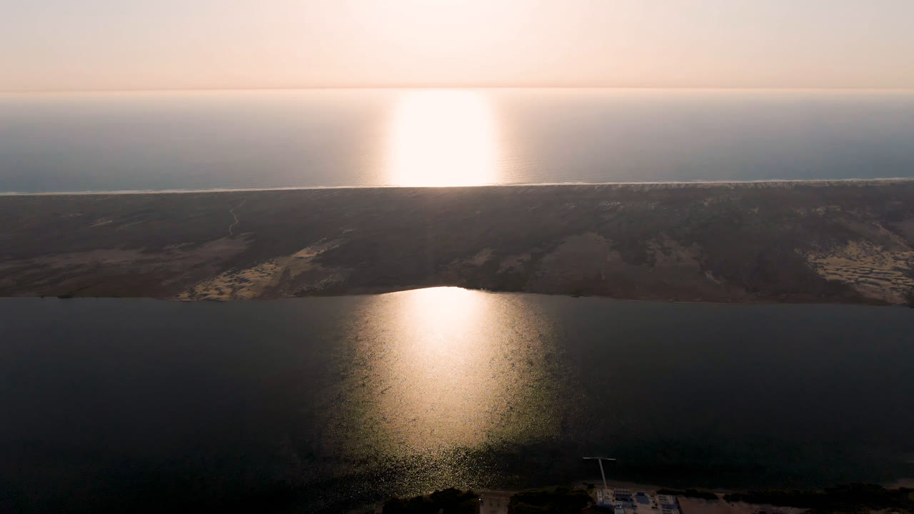 Aerial view in Aldofo Lopez Mateos, Baja California Sur, Mexico, with a broad dark water surface, a centered column of sun glare, sandy shoreline, and no visible people.