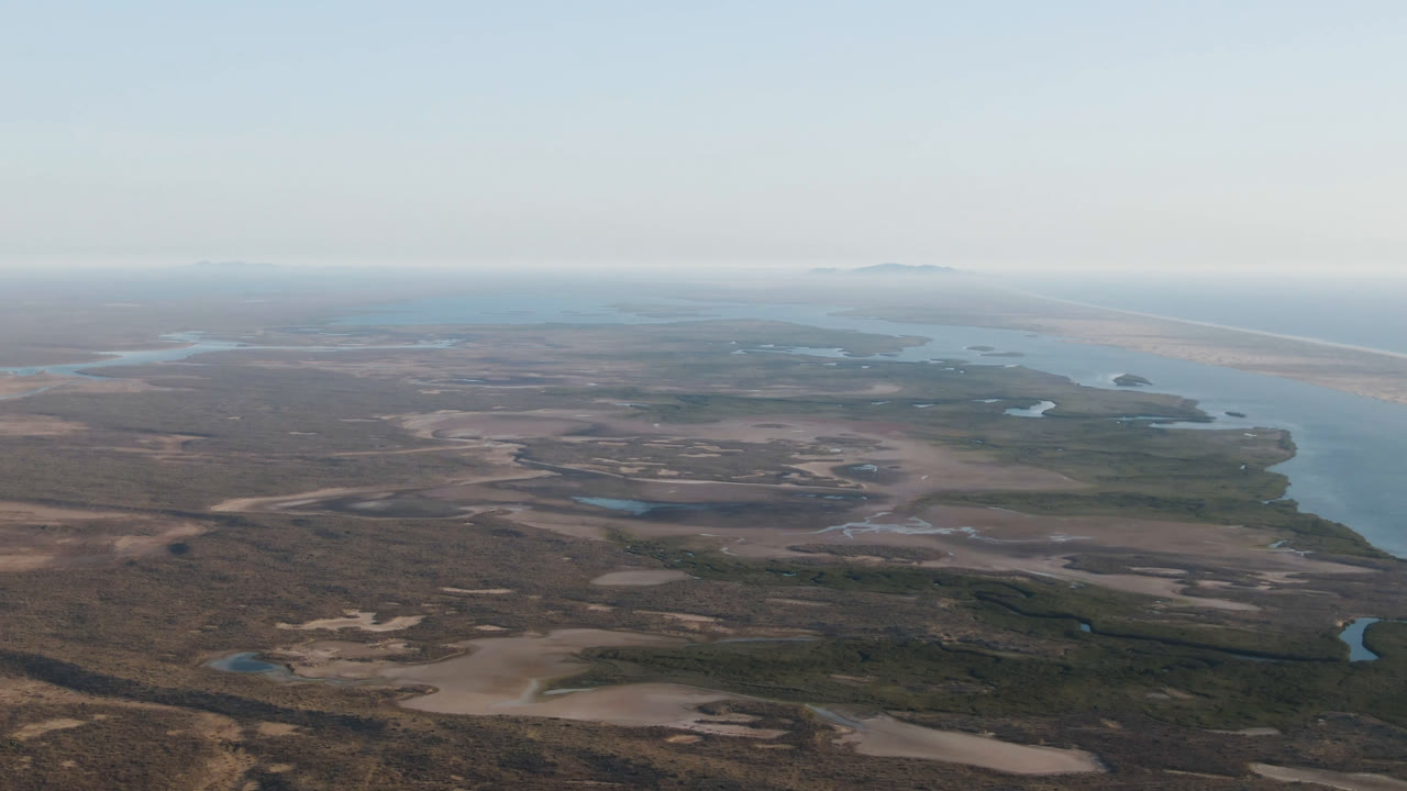 High aerial view of lagoon edge, sandy land, ocean, and distant low islands.