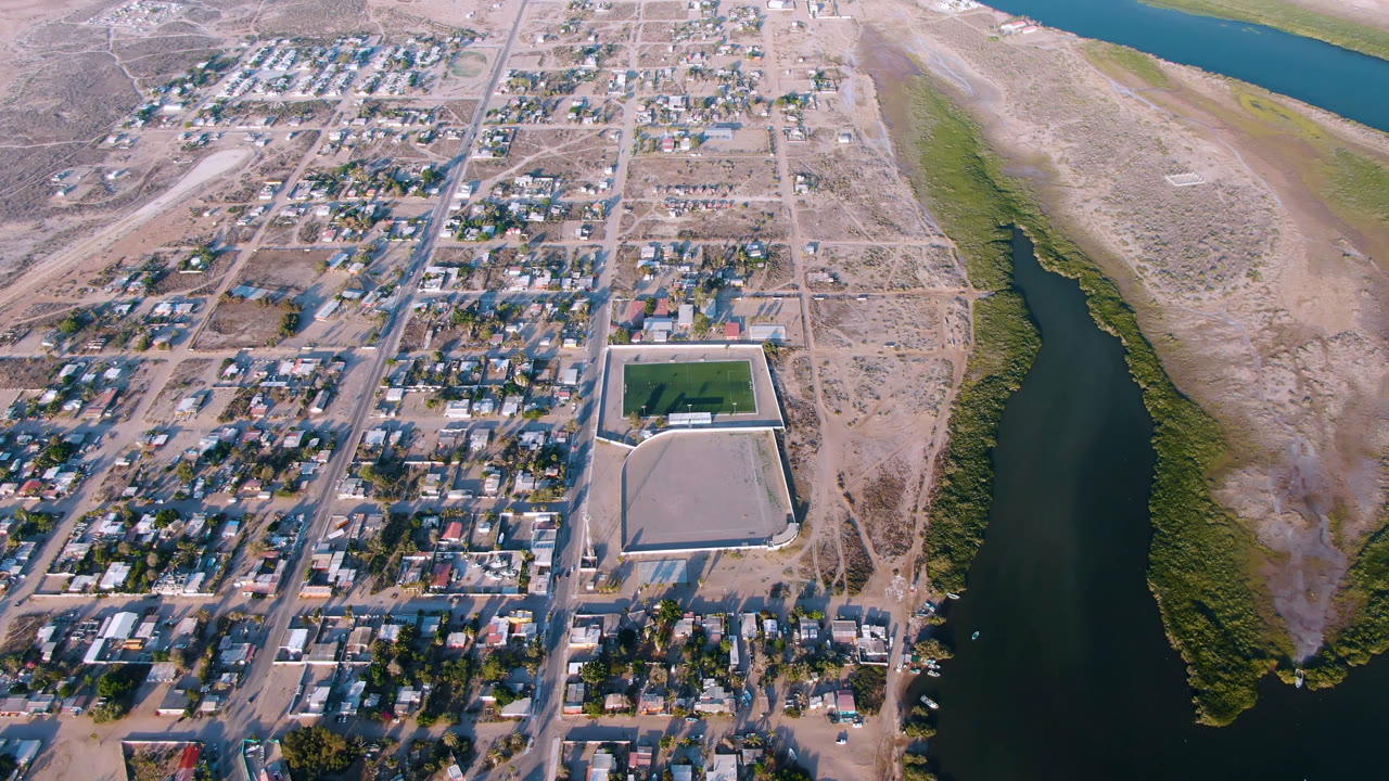 Aerial view of a town grid beside a river channel and dry scrubland.