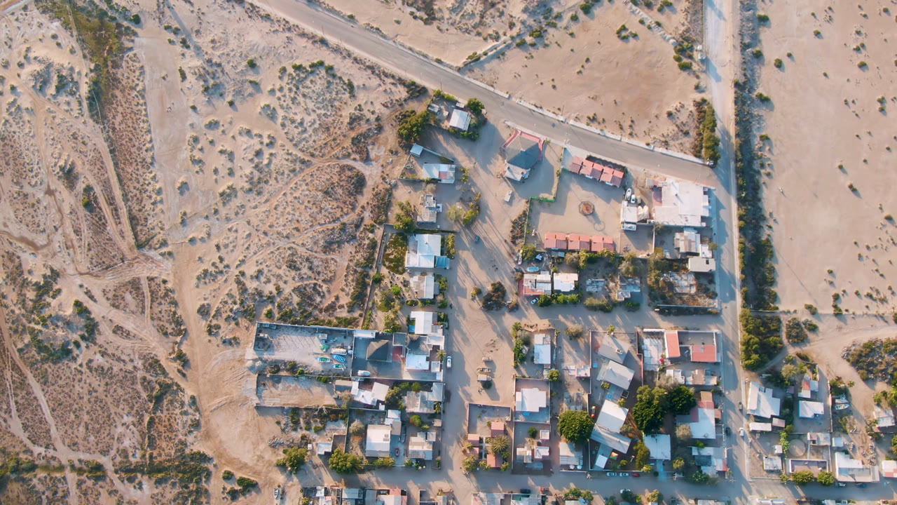 Overhead frame of Aldofo Lopez Mateos, Baja California Sur, showing low buildings, pale roads, scrubland, and no visible people at the start of the clip.