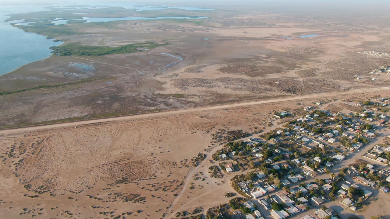 Aerial view of a small settlement beside sandy undeveloped land and blue river water.