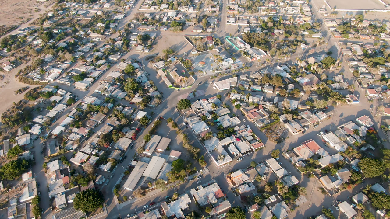 Overhead aerial view of houses, streets, trees, and sandy open ground.