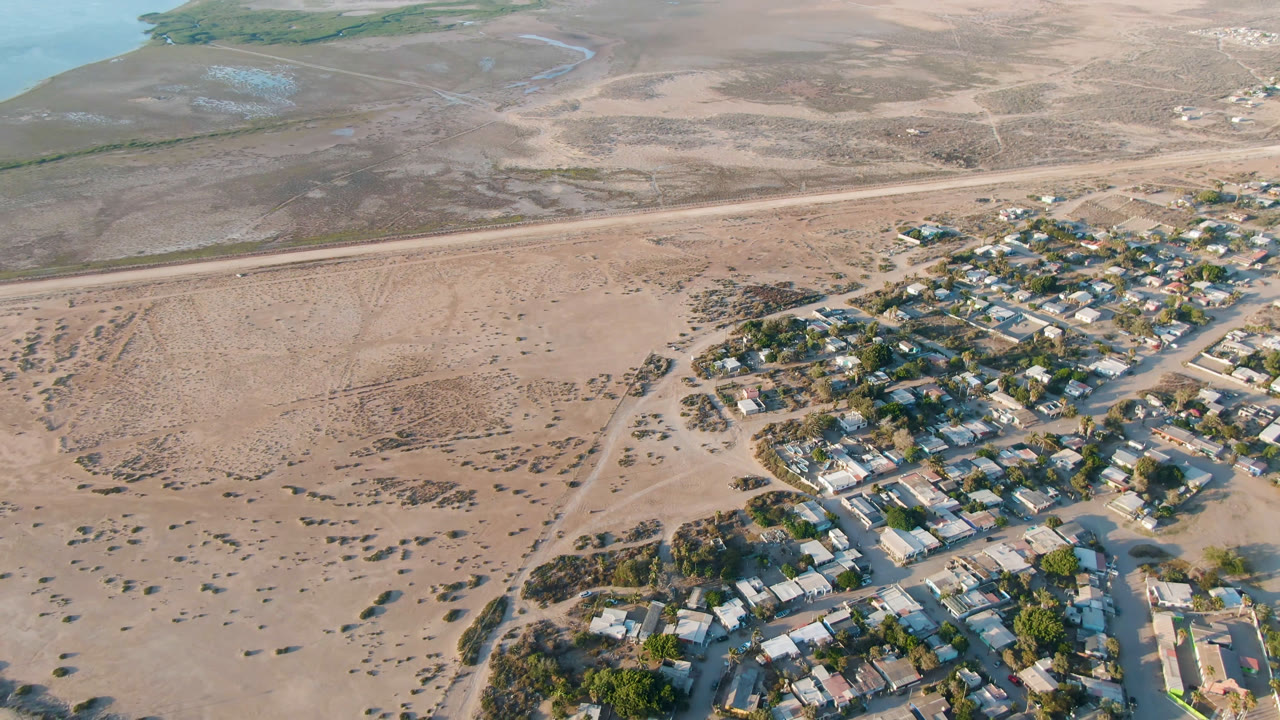 Aerial view of houses beside open sandy land and a straight road