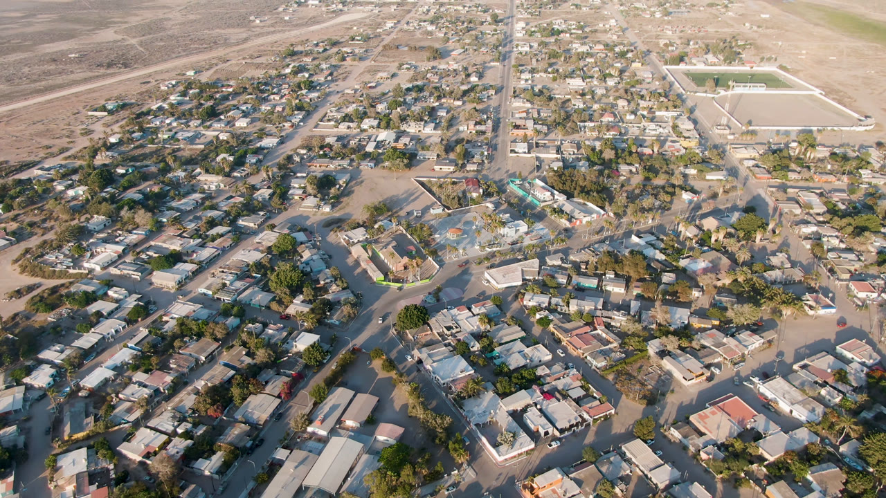 Aerial view of a compact town with houses, roads, desert land, and distant water.