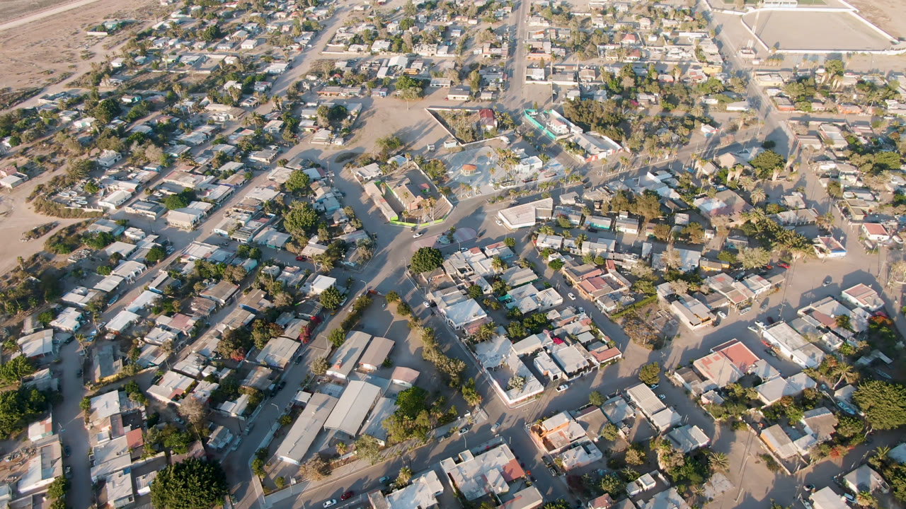 Aerial view over residential blocks, sandy roads, trees, and wet areas near the edge of town.