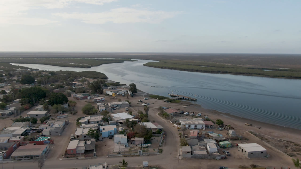 Aerial view of low homes beside a wide river and mangrove flats.
