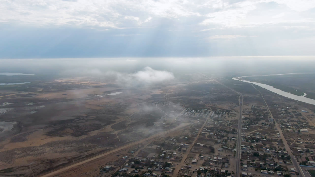 Drone-height view of a small town near a river under bright haze.