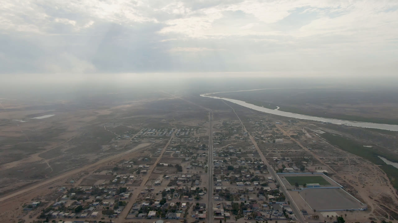 Aerial view of a small town beside a winding river under clouds.