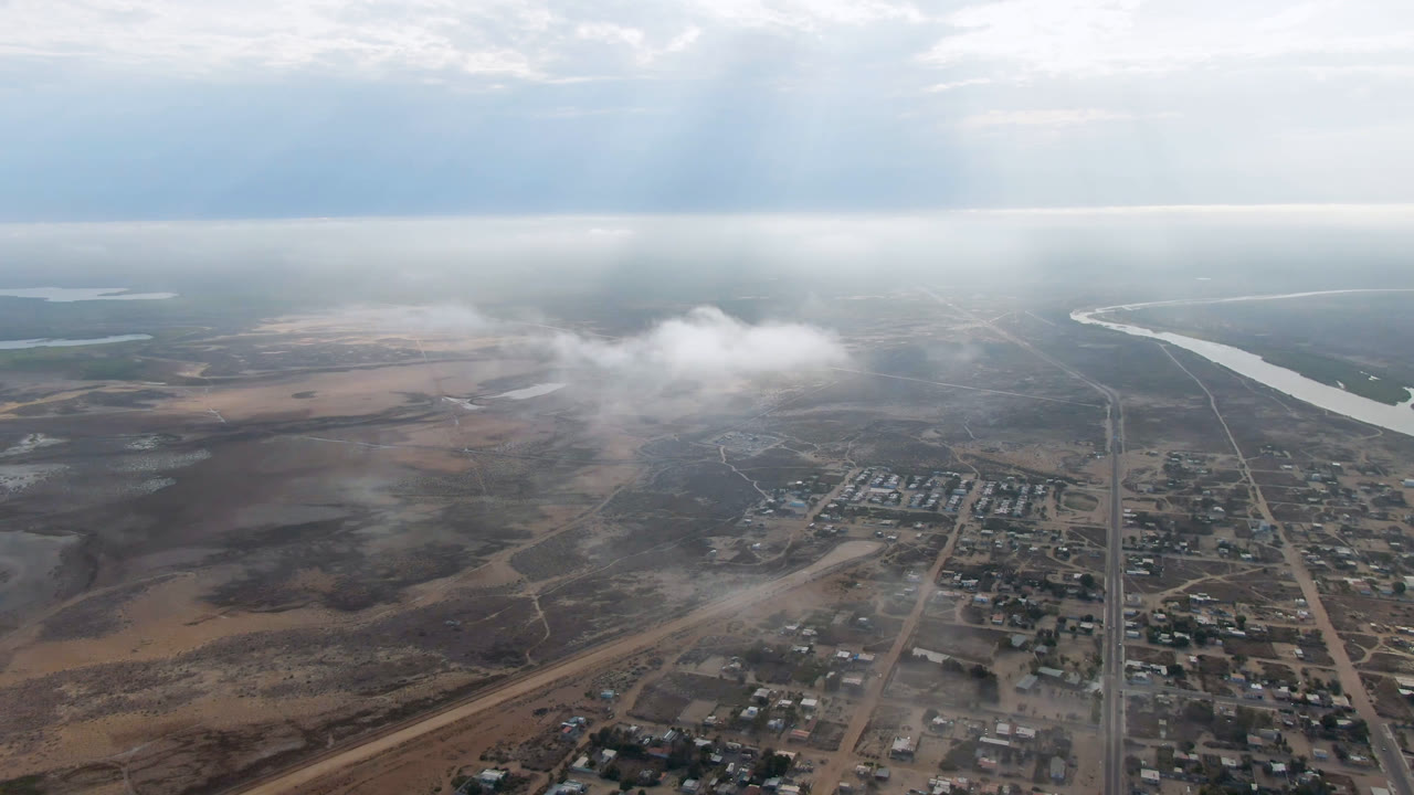 Town edge and dusty open land below a pale cloud layer