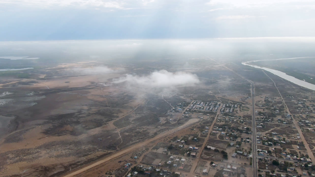 High aerial view of a dusty town, roads, low cloud, and distant river