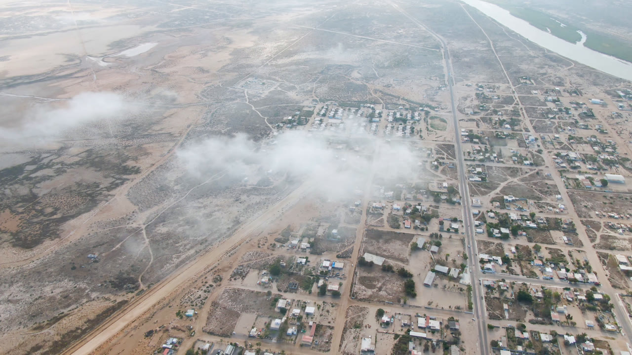 High aerial view of dry town blocks, roads, river edge, and white dust or cloud.