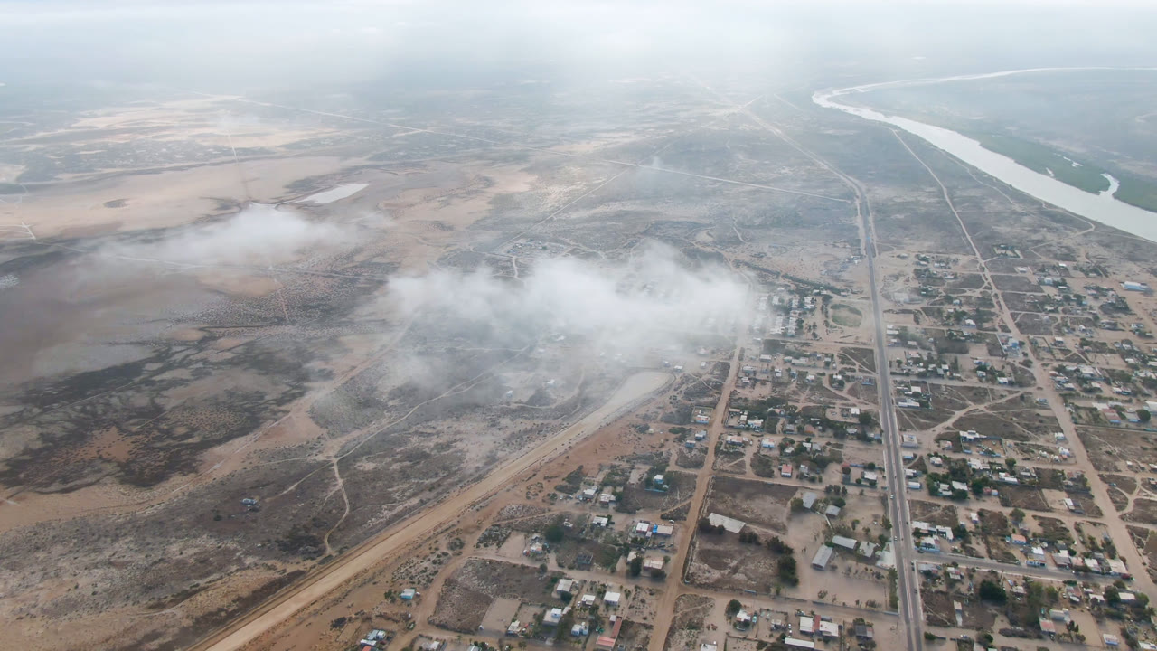 Hazy aerial view of a small town, roads, dry land, and a river in the distance.