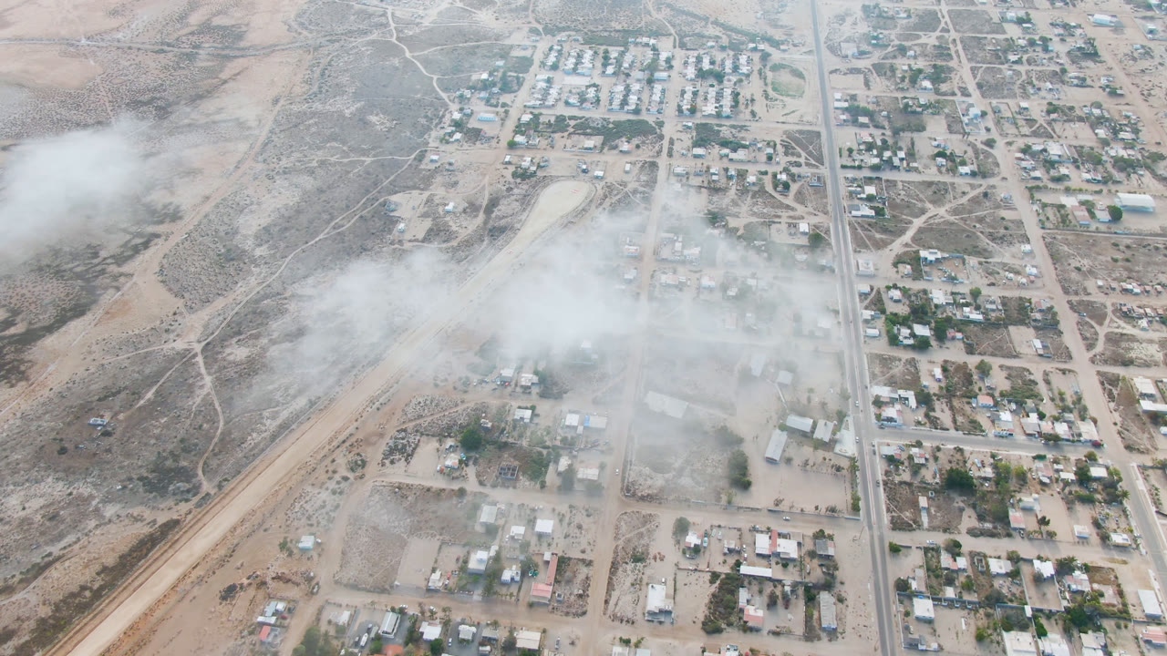 Dusty aerial view of a desert town with a road grid, buildings, and haze.