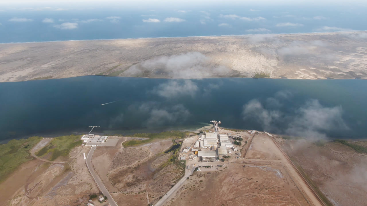 Aerial view of desert roads, shoreline buildings, dark water, and distant arid land.