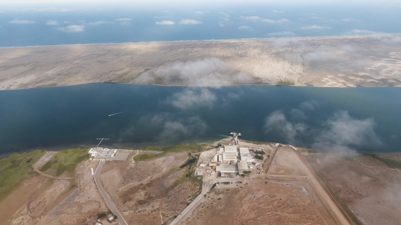 Aerial frame over Aldofo Lopez Mateos with the waterfront facility centered lower in frame, desert flats on both sides, dark water beyond, and no visible people.