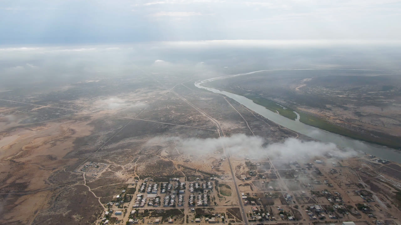 Second frame above Aldofo Lopez Mateos shows the river running diagonally past roads and clustered buildings, with a low cloud band crossing the town and no visible people.