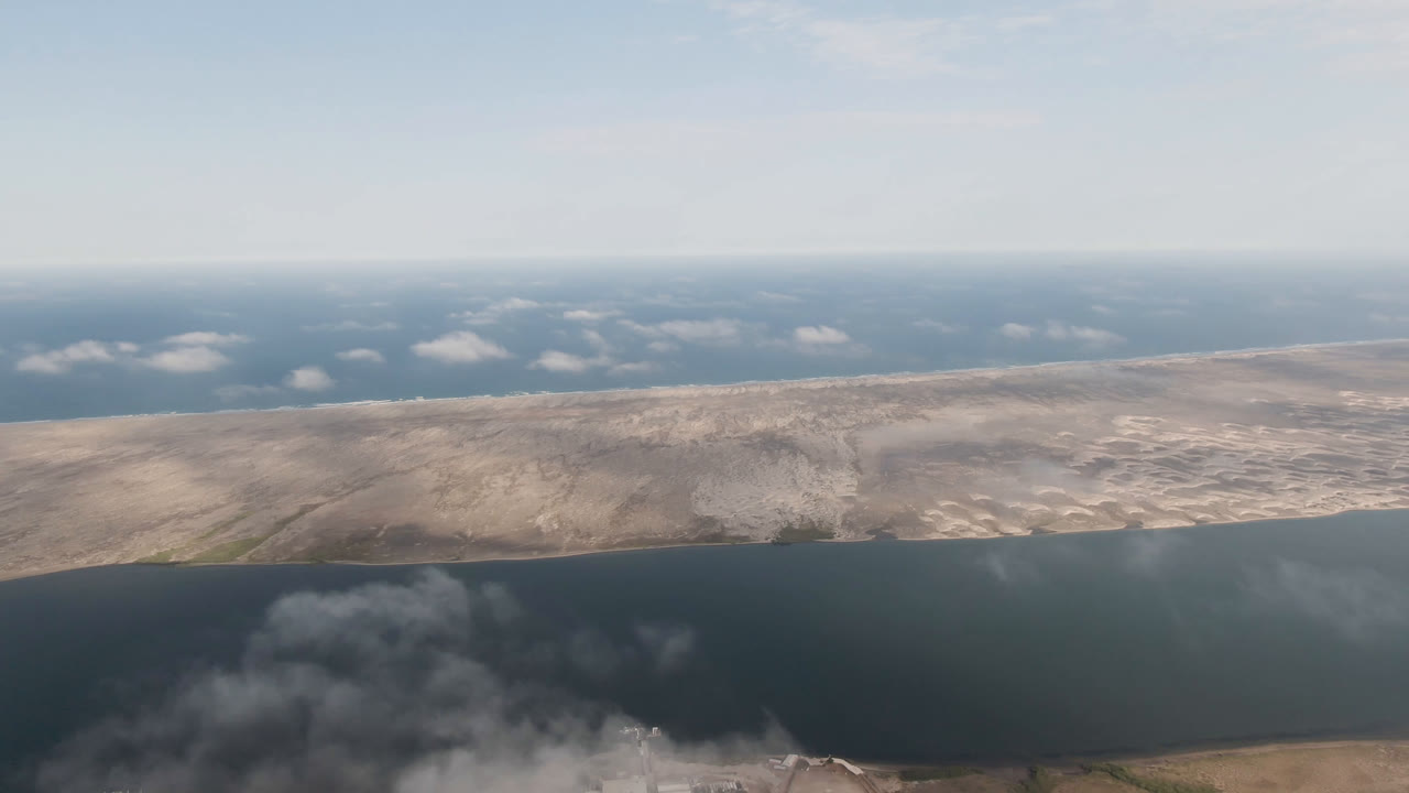 High aerial view of arid terrain bordered by dark water and low clouds.