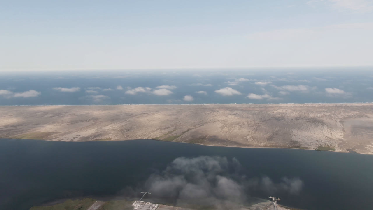 Aerial view in Aldofo Lopez Mateos, Baja California Sur, Mexico, showing dark lagoon water, pale coastline, open sky, and small waterfront structures partly visible at the lower edge with no visible people.
