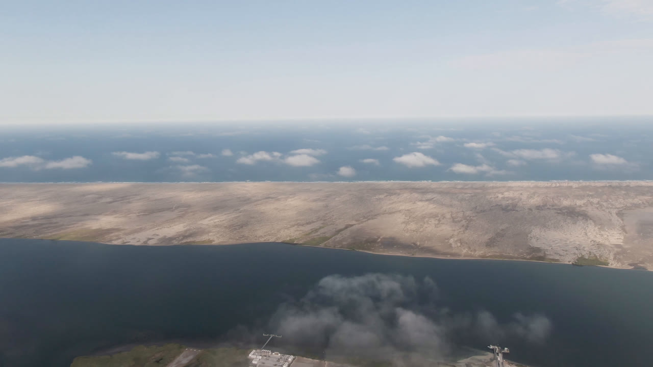 Aerial coastal water scene with cloud shadow over the foreground and pale land beyond.