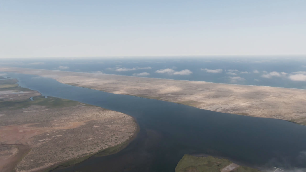 High aerial view of a broad river beside pale desert flats and low clouds.