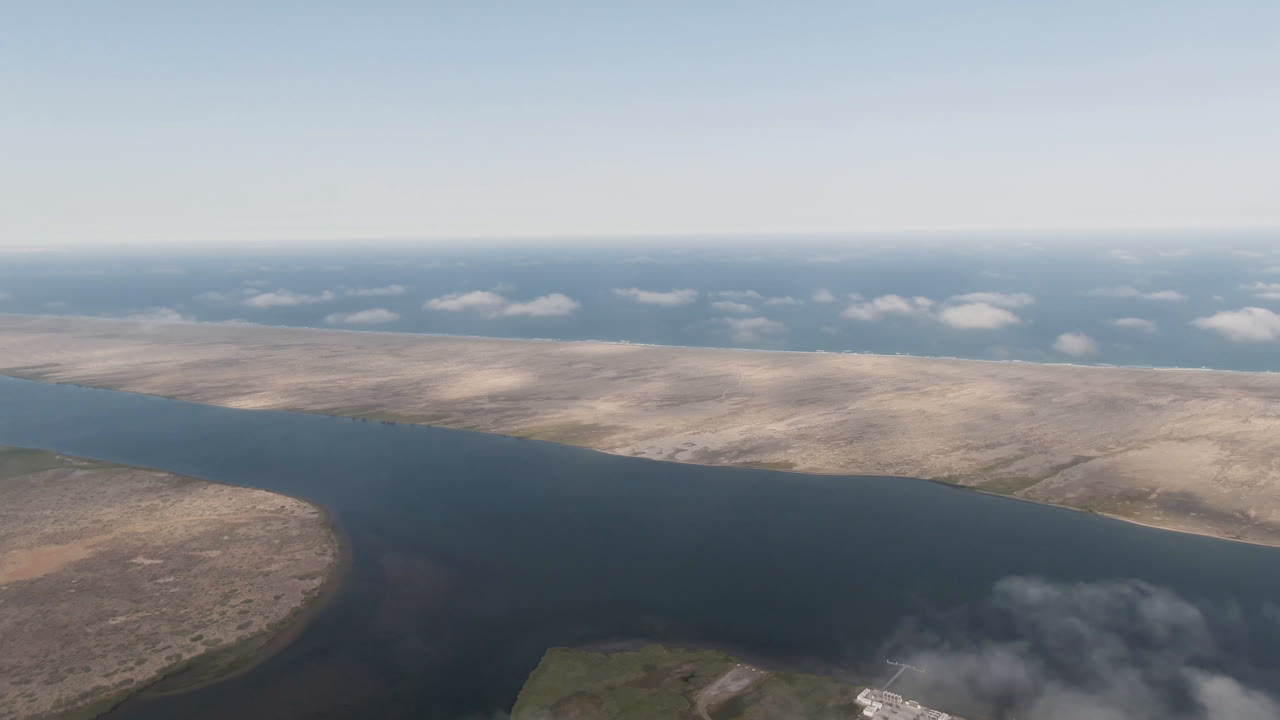 Aerial view over Aldofo Lopez Mateos, Baja California Sur, with a dark blue water channel curving past dry tan shoreline and no visible people.