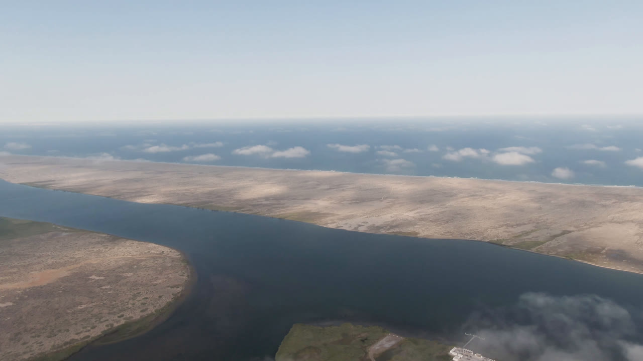 Aerial frame from Aldofo Lopez Mateos showing blue water across the middle of the image, pale sand flats beyond it, low clouds near the horizon, and no visible people.
