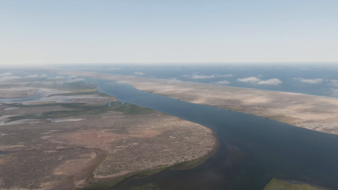 Wide aerial view of a river running through dry desert flats under blue sky.