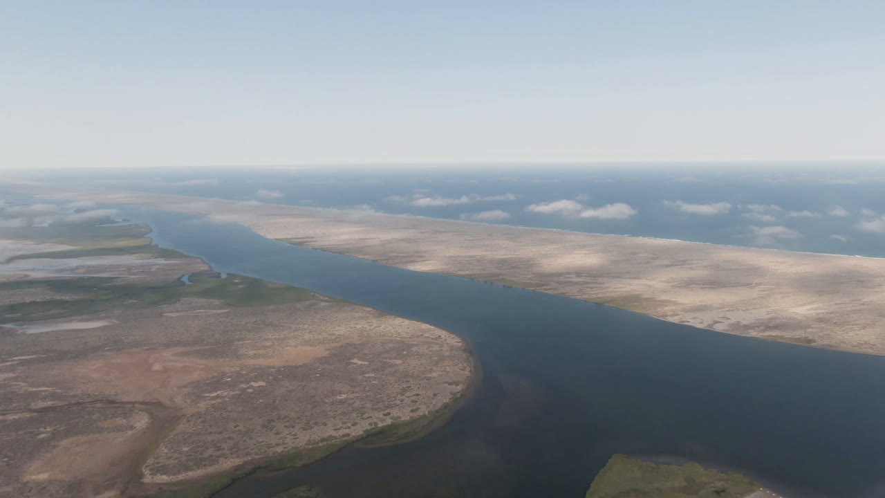 Aerial frame in Aldofo Lopez Mateos showing the river channel wider across the center, reddish desert ground in the lower left, bright sand flats to the right, and no visible people.