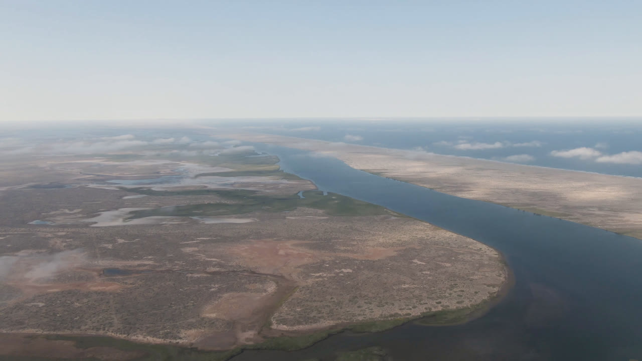 High view of blue water winding past sandy desert ground