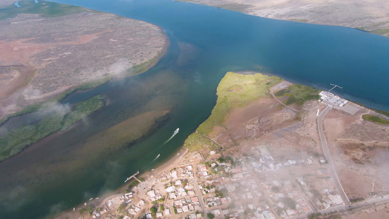 Aerial view of blue-green water, sandbars, docks, roads, and a small town edge.