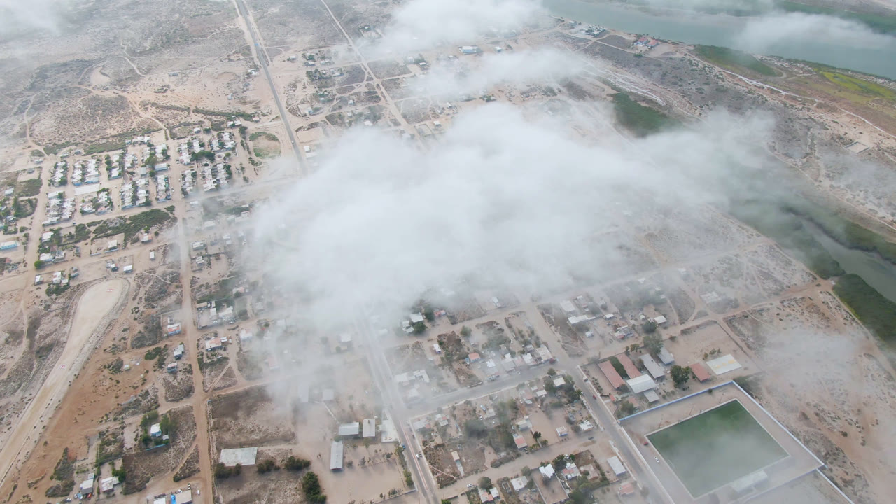 Aerial view of town streets, river water, and low cloud cover.