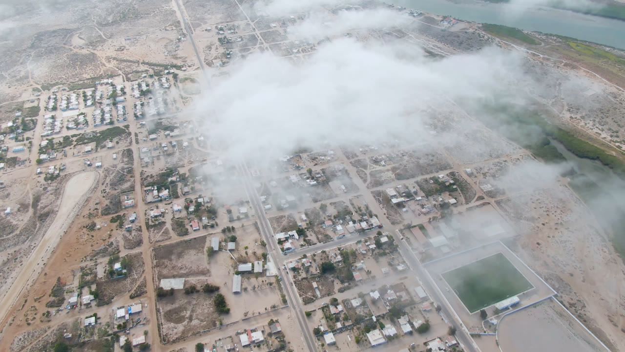 Aerial town grid beside water with low cloud over roads and homes.