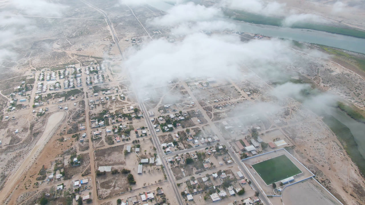 Aerial view of a small town, roads, river channels, desert terrain, and low fog.