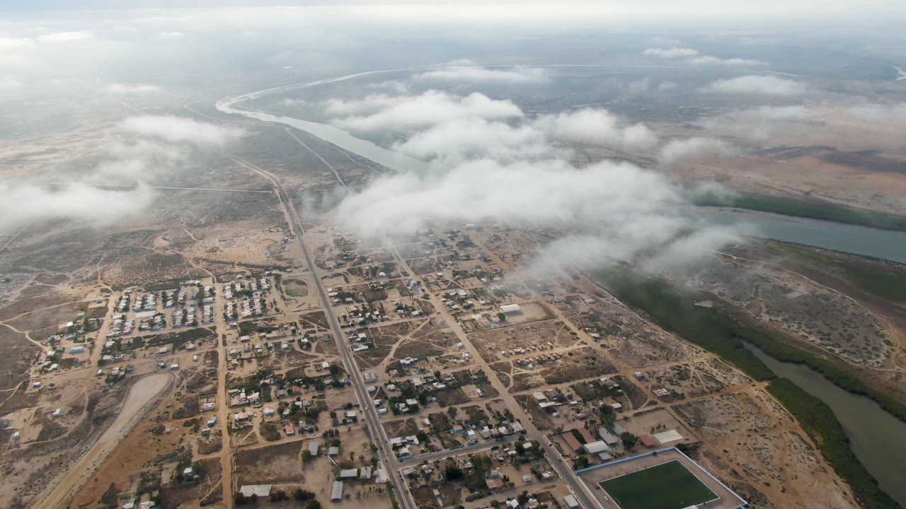 High aerial view of a dry town beside a winding river under low clouds.