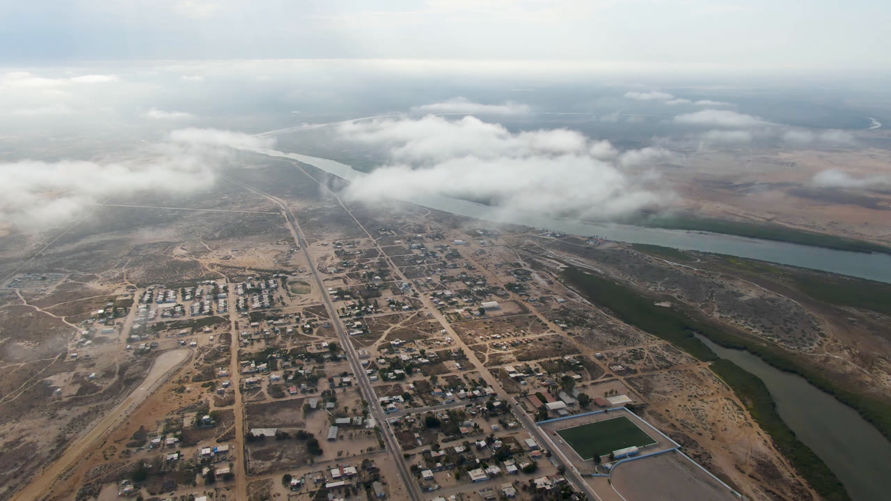Aerial view of a small town beside a winding river under low clouds.
