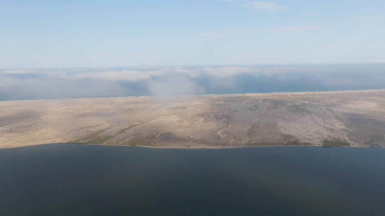 Aerial frame from Aldofo Lopez Mateos showing the sandy midground shifted slightly across the water, with a soft cloud bank over the horizon and no visible people.