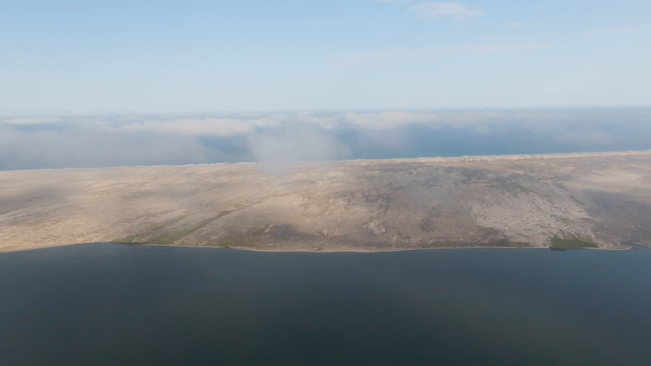 Distant sandy land across blue water with haze near the horizon.