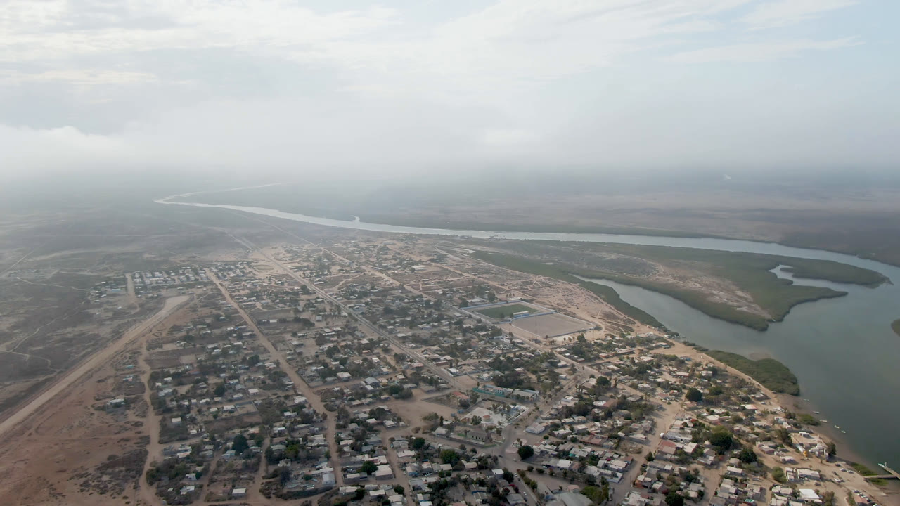 Aerial view of a small town beside a winding river under hazy daylight.