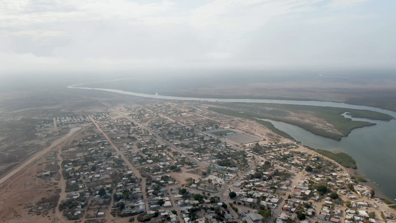 Aerial view of a village beside a winding river under cloudy sky.