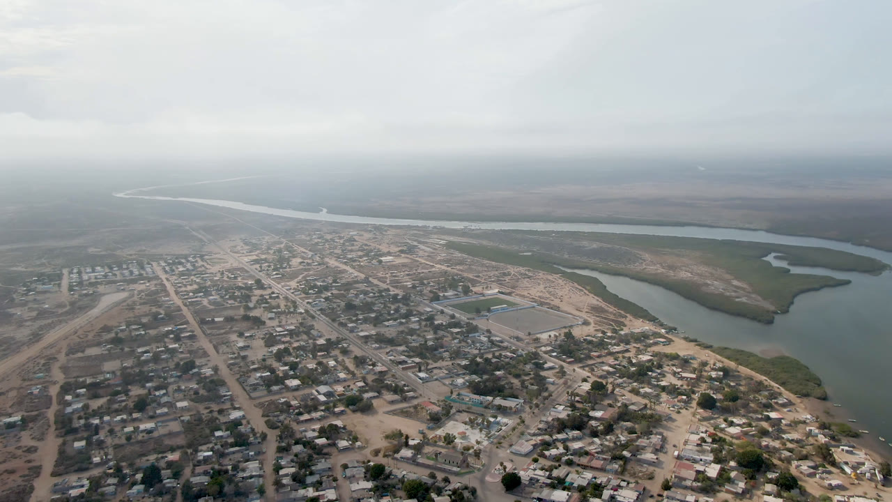 Aerial view of a village beside a winding river under hazy sky.