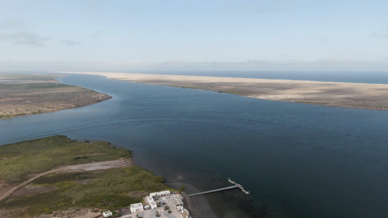 High aerial view across open water toward sandy coastline and horizon.